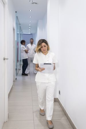 Female doctor walking in clinical corridor while holding a medical folder with medical team in the background
