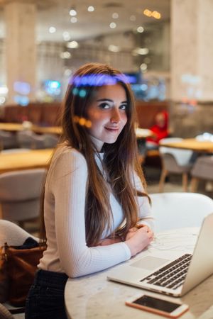 Woman smiling while looking up from laptop in a cafe