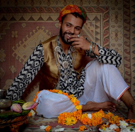 Man in traditional outfit smiling and  sitting on floor
