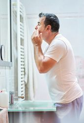 Man touching face in bathroom while looking in mirror