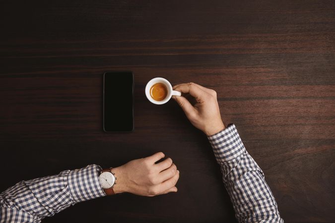 Top view of arms in plaid with espresso shot and cell phone