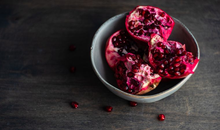 Ceramic bowl of open pomegranates on wooden table