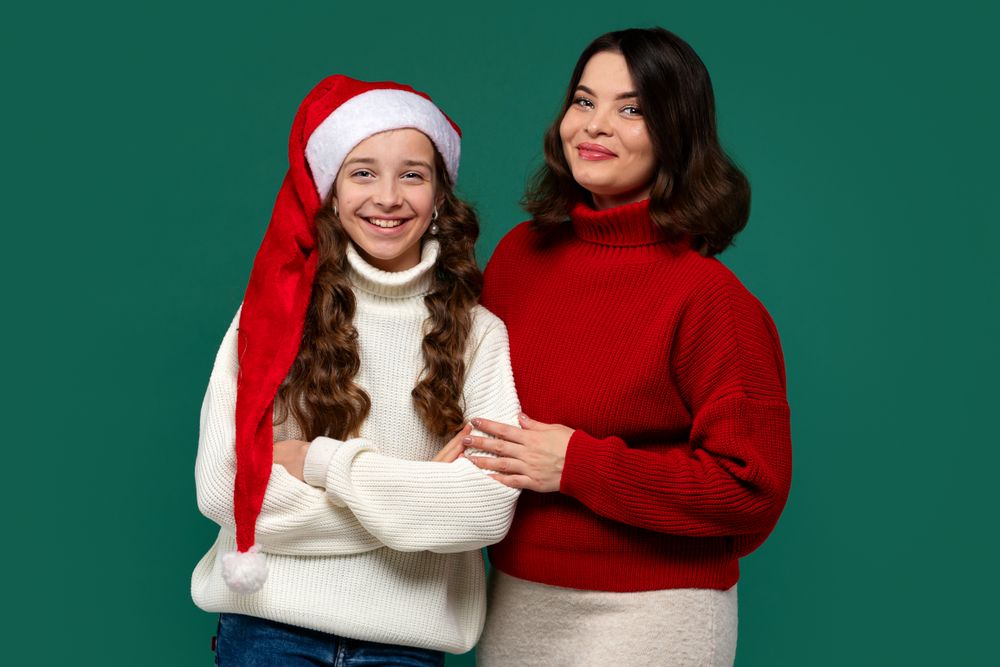 Mum and teenage daughter pose in holiday sweaters, smiling happily