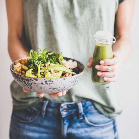 Woman standing holding vegetarian bowl and green smoothie
