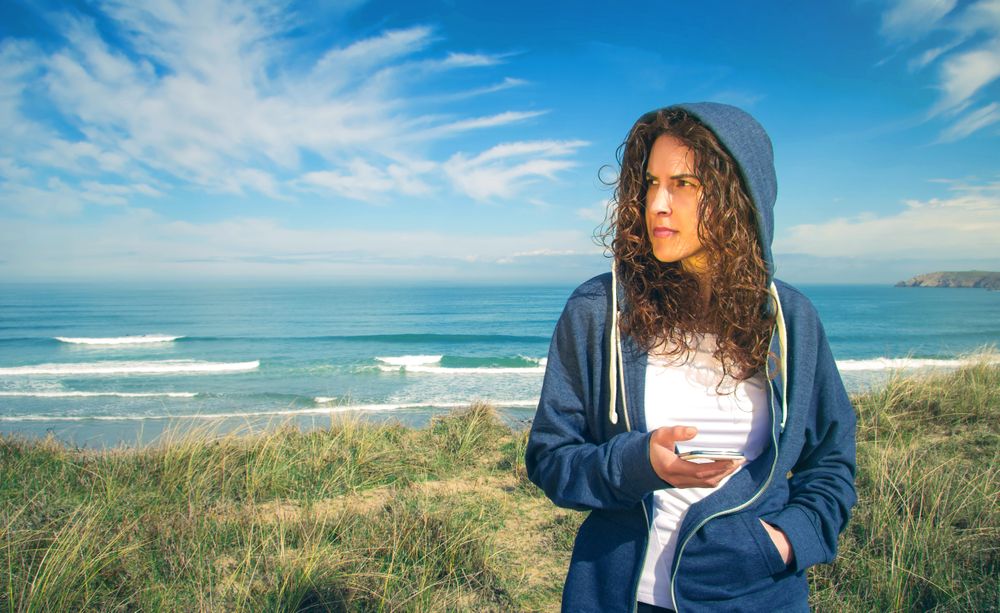 Woman checking phone with ocean waves in background