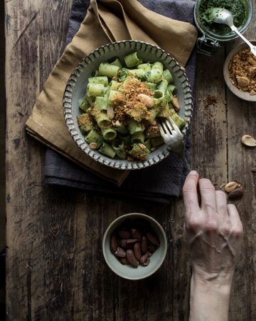 Hands taking pasta paccheri with kale pesto and nuts