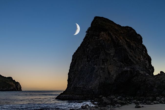 Crescent moon above quiet rocky beach at dusk