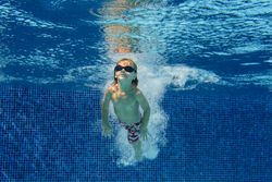 Adorable preschooler boy swimming in goggles underwater in pool