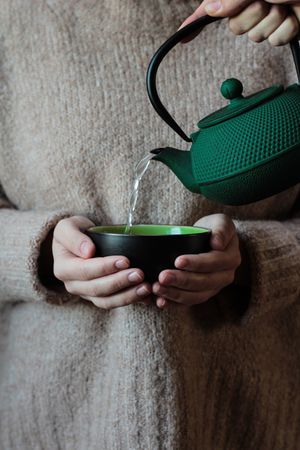 Person pouring tea to cup in hands of woman