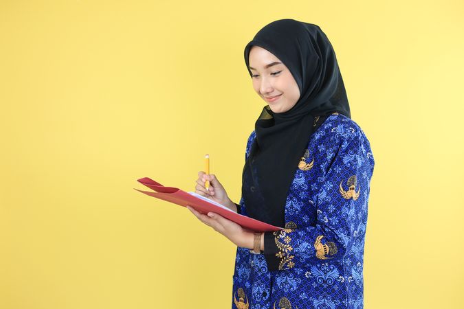 Young Worker Wearing Korpri Batik Uniform Holding Pencil, Checking Document Paper