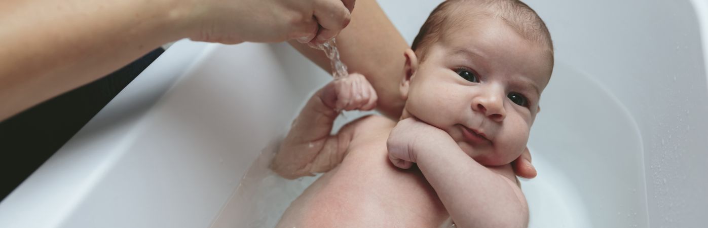 Newborn in the bathtub held by her mother