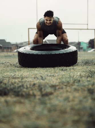 Energetic man using all energy to lift tire up during exercise