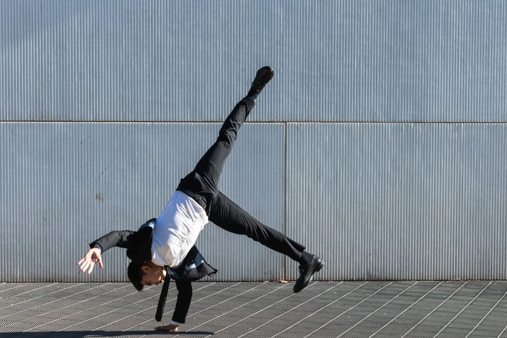Asian businessman performing breakdance handstand on street