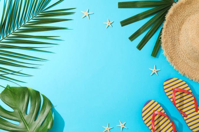 Palm leaves, flip flops, hat and starfishes on blue background, copy space