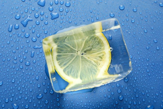Top view of large ice cube with lemon slice on blue table