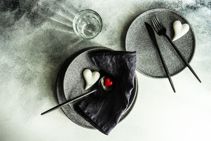 Two place settings for St. Valentine Day with hearts, dark cutlery and grey plates