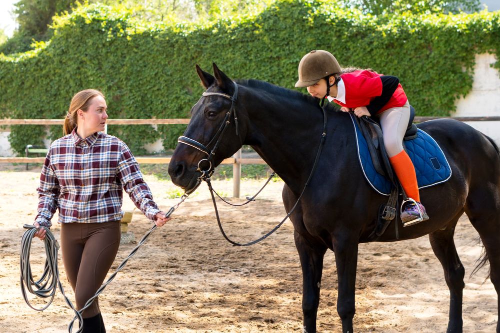 Instructor guides young rider in horse handling in riding arena.