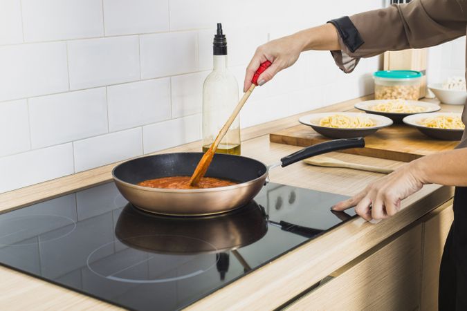 Person mixing sauce in pan on stove