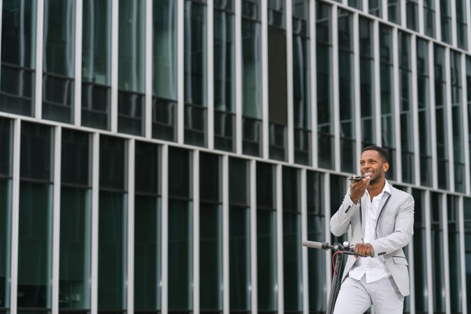 Smiling Black man riding scooter and speaking on smartphone