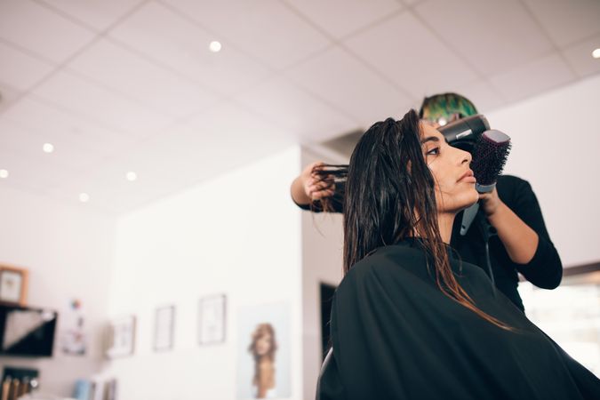Female hairstylist using hair blow dryer to dry client’s hair