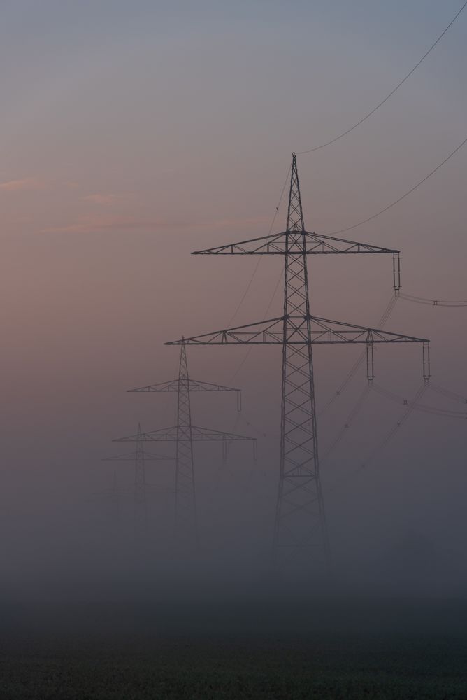 Electrical grid towers in a row on a foggy morning in a german village