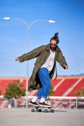 Stylish hipster in trench coat and jeans riding skateboard