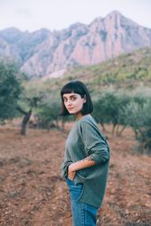Woman with hand in pocket in beautiful park with hills and olive trees