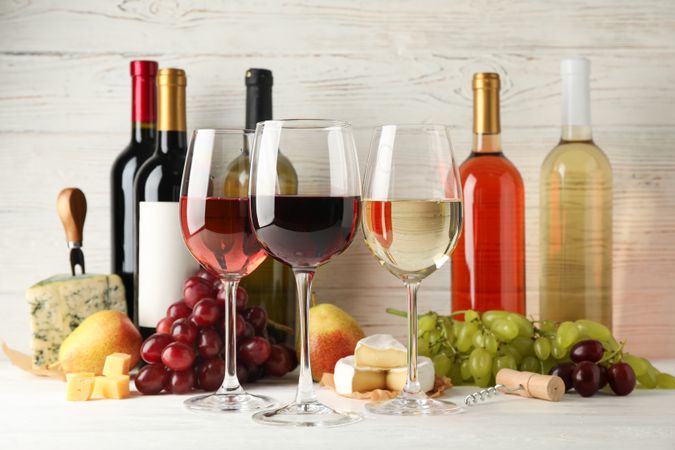 Fruits, cheese, bottles and glasses with different wine on blank background, space for text