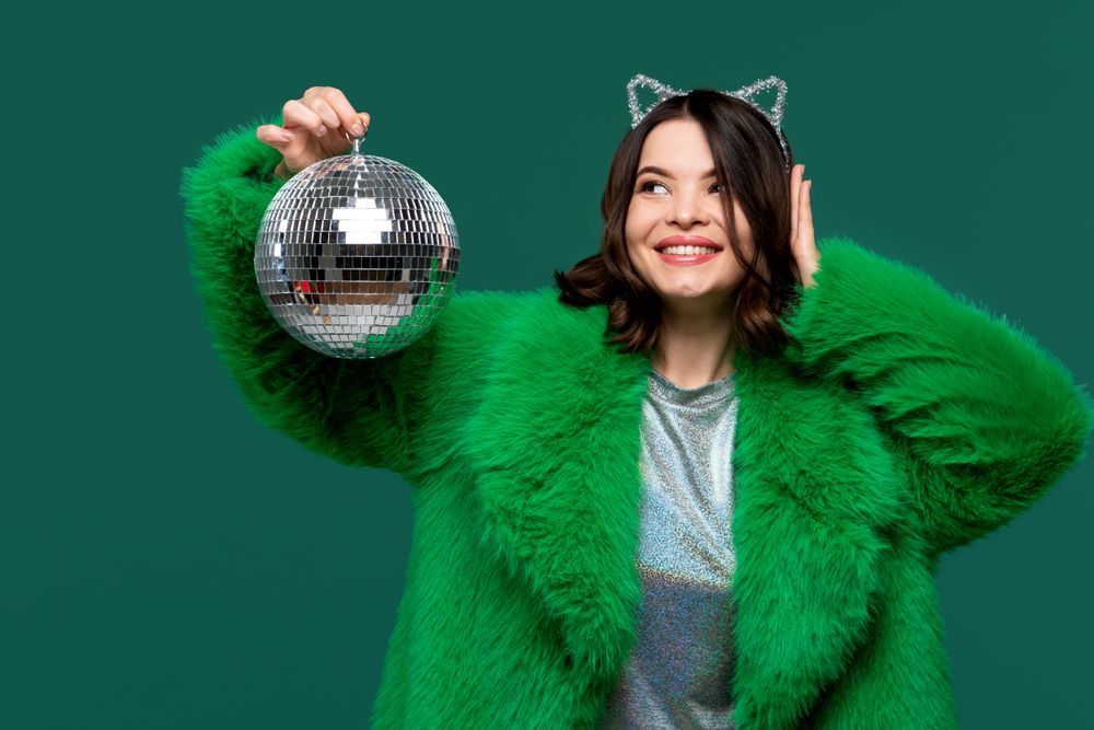 Cheerful woman in green fur coat holding disco ball.