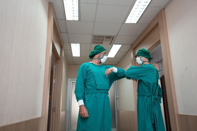 Two medical professionals in scrubs greeting each other with elbow bump