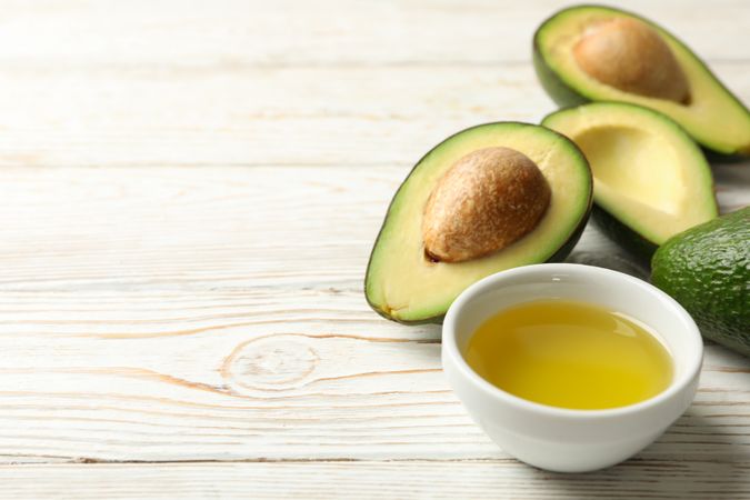 Ripe fresh avocado and oil on wooden background, close up