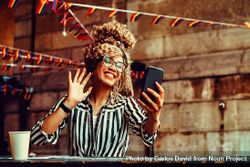 Smiling Black woman in stripe shirt waving at phone in cafe 4BpmW0