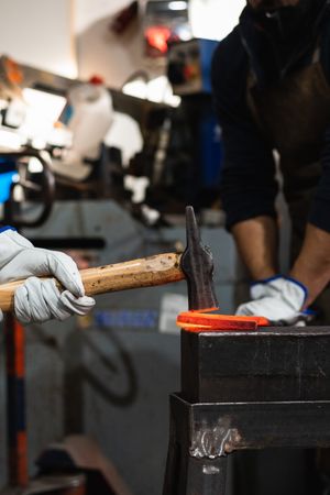 Blacksmiths forging hot metal with hammer in workshop