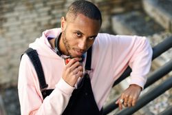 Pensive male in overalls and hoodie leaning on railing of stairs outside