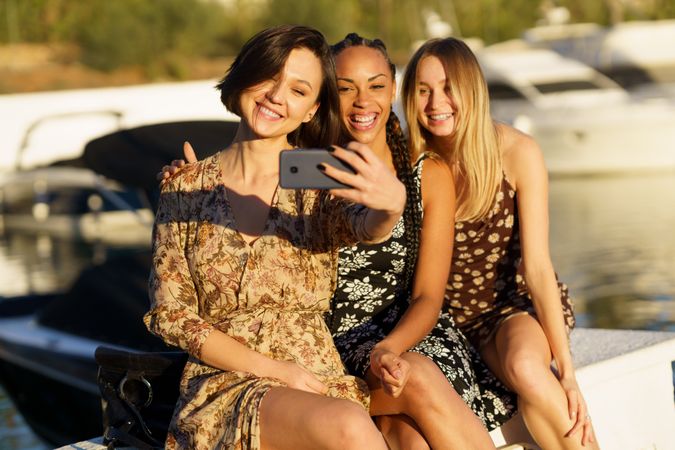 Three smiling women sitting on wharf taking selfie