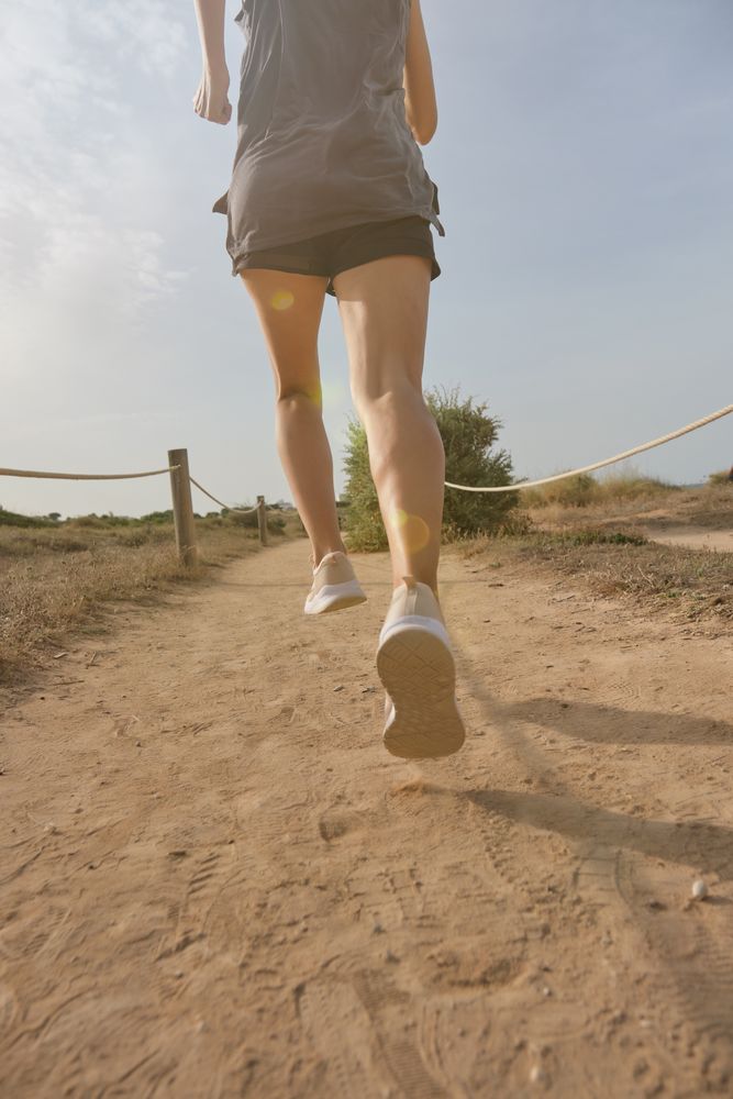 Unrecognizable woman jogging on sandy road