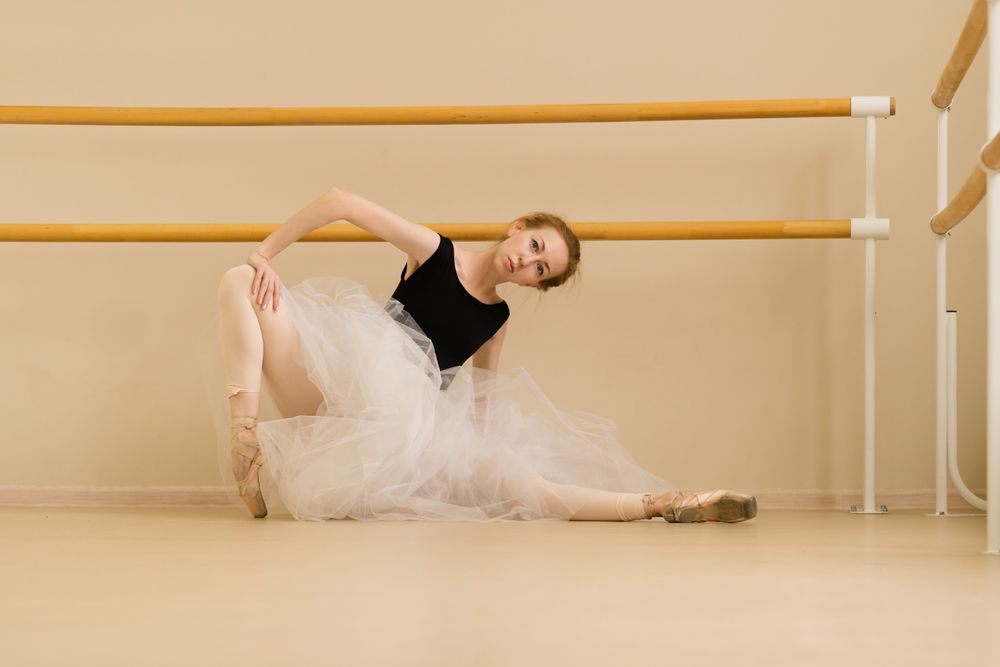 Ballet dancer performs dynamic stretch while seated on the floor