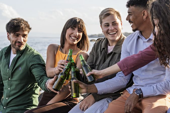 Multicultural friends cheering with beer bottles at seaside party at sunset