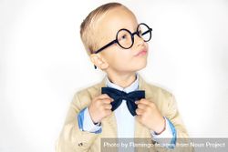 Serious blond boy in glasses fixing his bow tie looking away bEApMb