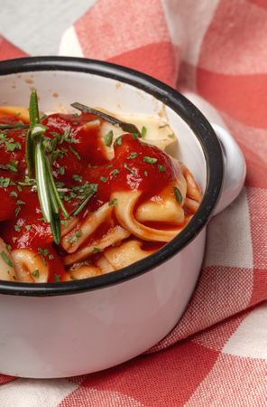 Bowl of delicious ravioli with tomato sauce and rosemary on table cloth