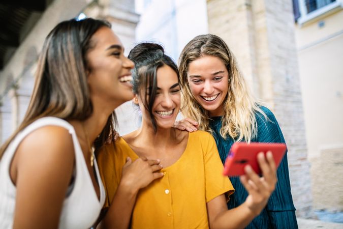 Laughing multi-ethnic friends looking at phone together outdoors