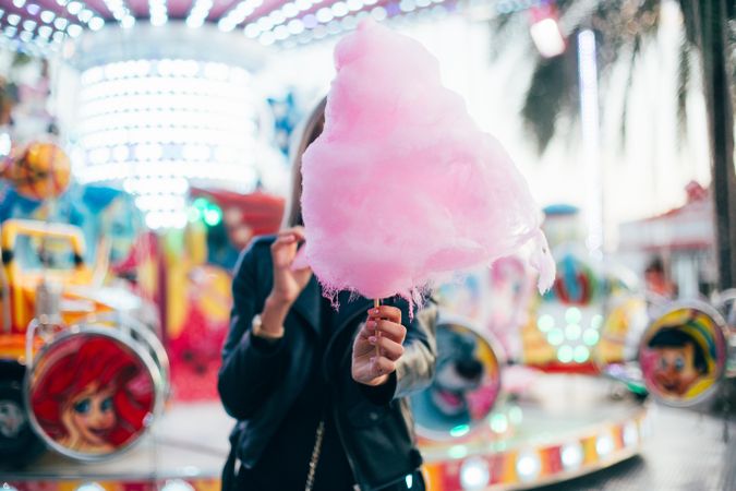 Woman covering face with large cotton candy outside of fairground ride