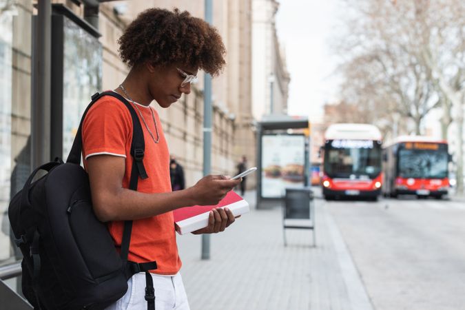 Black male student waiting for bus on street