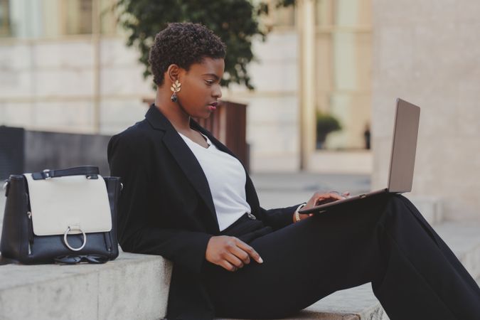 Stylish Black woman with laptop on steps near handbag