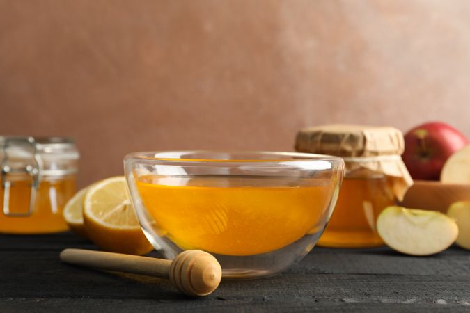 Bowl with honey, dipper and fruits on wooden background, space for text