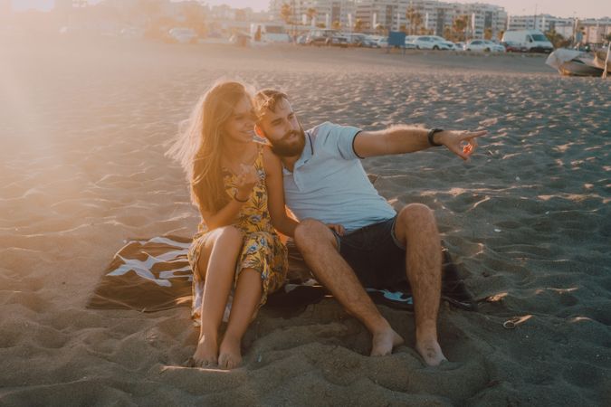 Tender couple talking and pointing in sunlight on towel beach