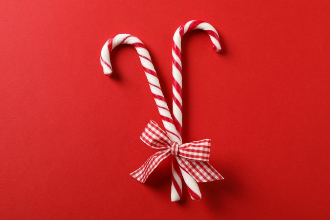 Sweet candy canes with bow on red background, space for text