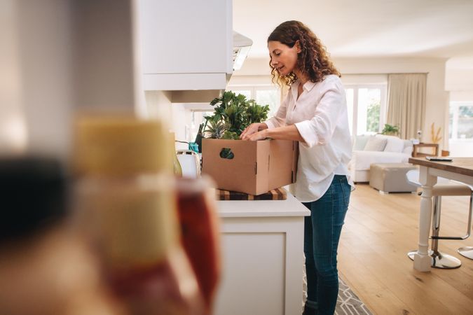 Woman looking in the box of groceries from delivery in her kitchen