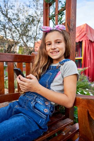 Smiling girl with smartphone sitting on bench
