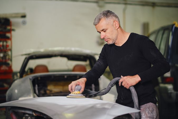 Mechanic grinding paint from car detail